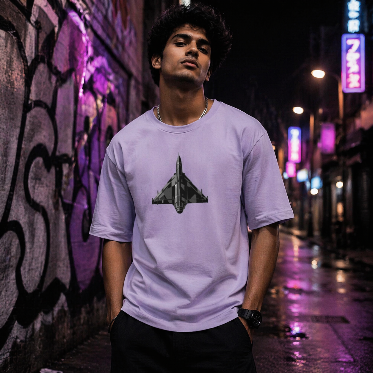 Person wearing a light purple t-shirt with a fighter jet graphic in an urban setting at night.